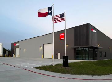 Edificio industrial moderno con fachada gris con banderas de Texas y Estados Unidos al frente.