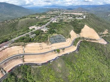 Vista aérea de una carretera montañosa con curvas, taludes de tierra y vegetación alrededor.