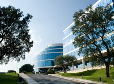 Fachada acristalada de la sede de Devicare en España, en un entorno ajardinado con árboles y zonas verdes.