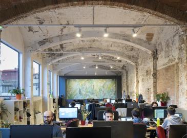 Oficina amplia de estilo industrial con varias personas trabajando frente a ordenadores.