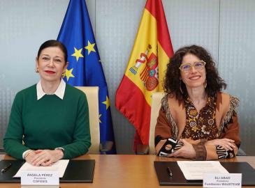 Dos mujeres sentadas a una mesa, con un documento delante, posando para una foto.
