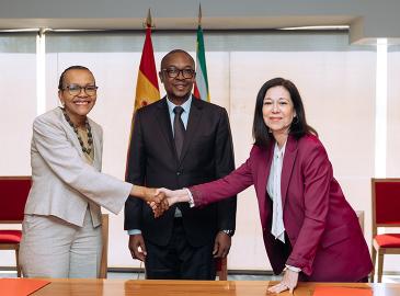 Dos mujeres estrechándose la mano ante un hombre, posando para la foto. 