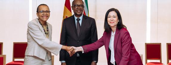 Dos mujeres estrechándose la mano ante un hombre, posando para la foto. 