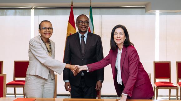 Dos mujeres estrechándose la mano ante un hombre, posando para la foto. 